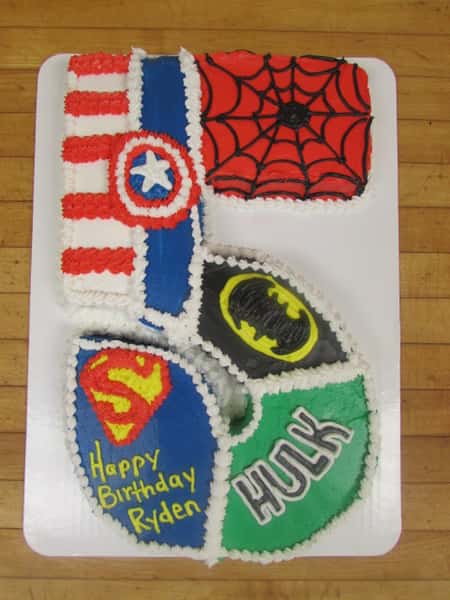 Cake in the shape of a five that is decorated into different sections to represent superman, the hulk, batman, captain america and spider man.