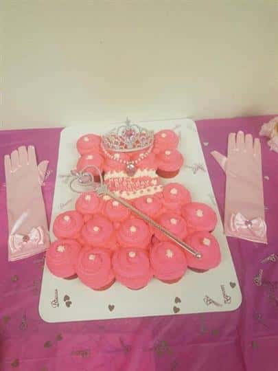 pink cupcakes lined up to look like a dress with a tiara and wand on top and pink silk gloves by the side