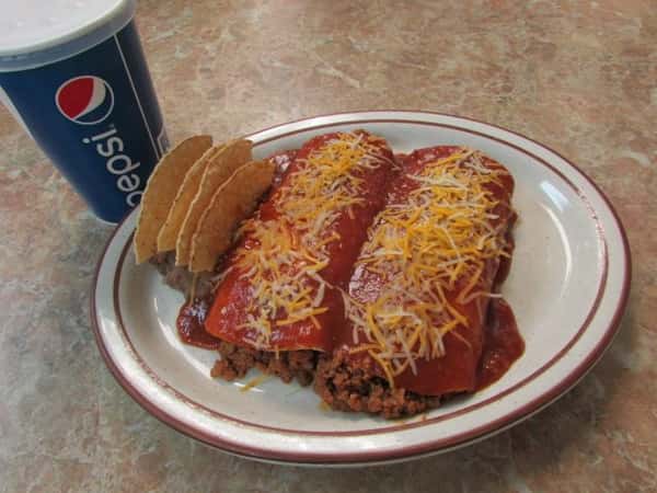 Two tortillas stuffed ewith seasoned ground meat smothered in sauce and cheese with refried black beans and tortilla chips on the side