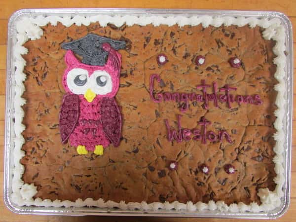 Rectangle cookie cake that says Congratulations Weston on it decorated with a pink owl wearing a graduation cap