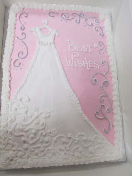 Pink frosted rectangle cake decorated with a hand drawn wedding dress in frosting that reads "Best Wishes"