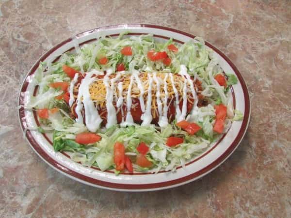 Bowl filled with shredded lettuce and diced tomatoes with a stuffed tortilla smothered in sauce, cheese and drizzled in sour cream, in the center.