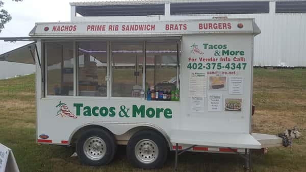 Tacos & More Food truck with sign reading " Nachos, Prime Rib Sandwich, Brats, Burgers" and "For Vendor Info Call 402-375-4347"