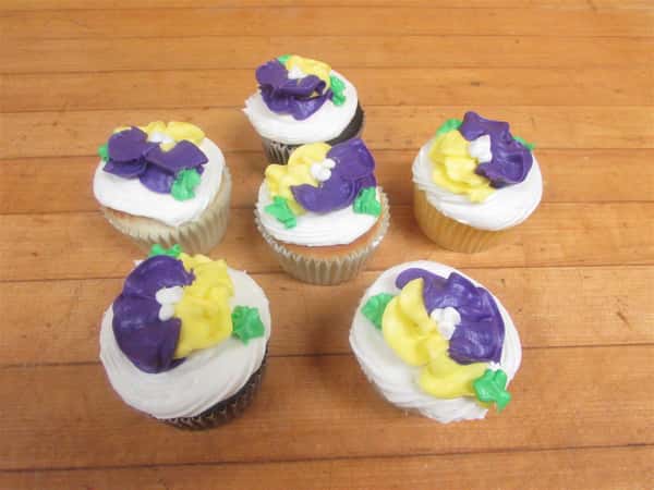 Six frosted cupcaked decorated with yellow and purple flowers made of frosting