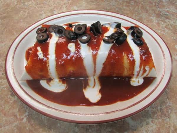 Stuffed flour tortilla smothered in sauce drizzled with sourcream and topped with sliced black olives