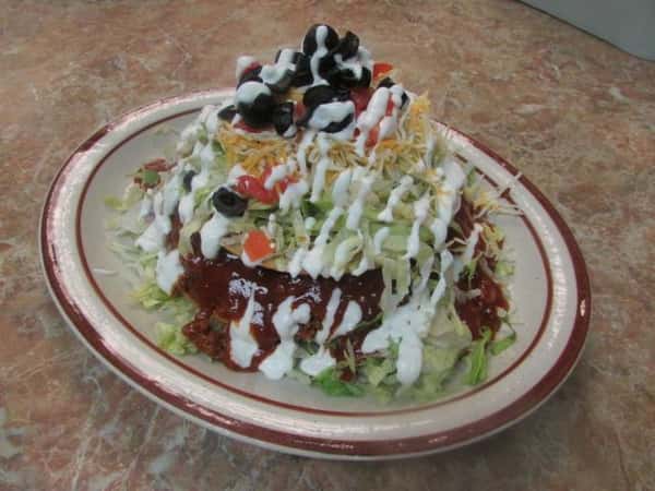 Salad made with shredded lettuce, ground meat, shredded yellow cheese, sliced black olives, diced tomatoes, drizzled in sour cream
