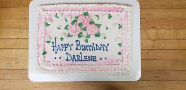 Rectangle cake decorated with pink and white frosted flowers that says Happy Birthday Darlene