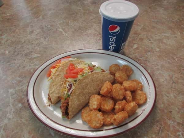 Two hard shell tacos filled with ground meat, tomatoes, shredded lettuce and cheese with a side of tater tots and a drink in a Pepsi to-go cup.