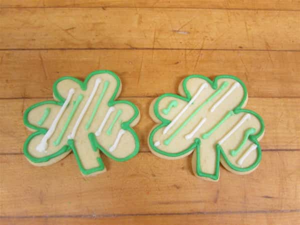 Two sugar cookies shaped like four leaf clovers with green frosting