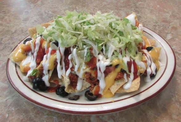 Loaded nachos with ground meat, nacho cheese, sliced tomatoes, sliced black olives topped with shredded lettuce and drizzled sour cream