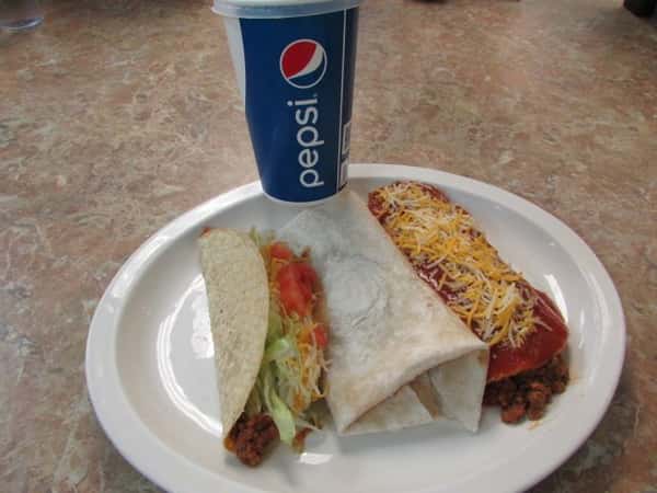 Hard shell taco with beef shredded lettuce and tomatoes, with a burrito and a tortilla stuffed with ground meat smothered in sauce and cheee with a soft drink in a Pepsi to-go cup
