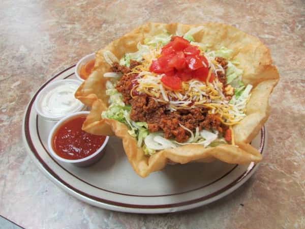 Ground seasoned beef lettuce, cheese, sauce & tomato in an edible tortilla bowl with a side of sour cream and salsa