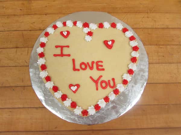 cake in the shape of a heart that sayas i love you in red frosting with a bordering of red and white frosting