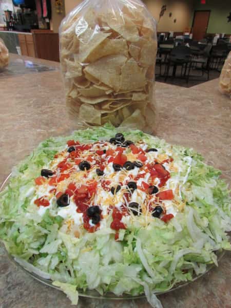 Plate of shredded lettuce toped with sour cream, salasa, diced tomatoes, sliced black olives and a bag og tortilla chips
