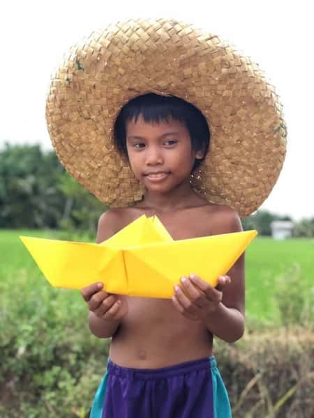 close up of child holding a yellow origami boat