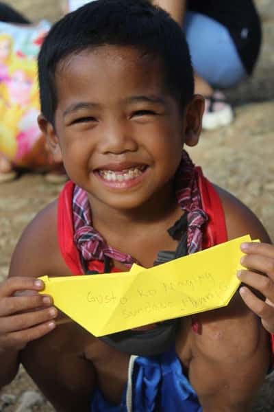 close up of child holding a yellow origami boat