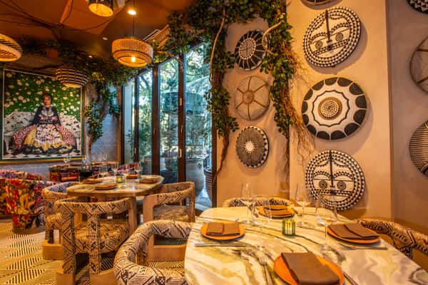 Eclectic restaurant dining area with patterned decor, woven wall art, marble tables, and warm ambient lighting