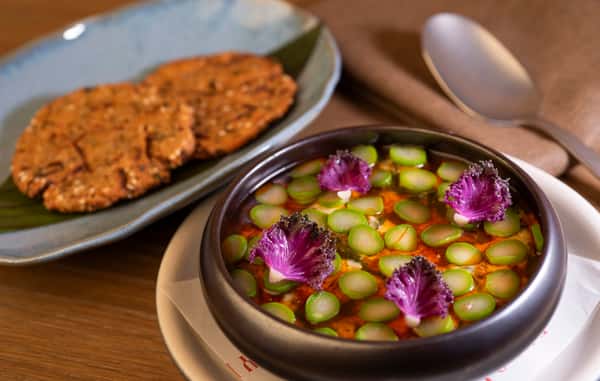 Colorful vegetable curry topped with asparagus and edible flowers served alongside crispy flatbread
