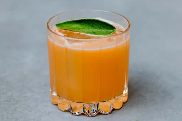 Orange craft cocktail served over ice with fresh sage garnish in a crystal rocks glass