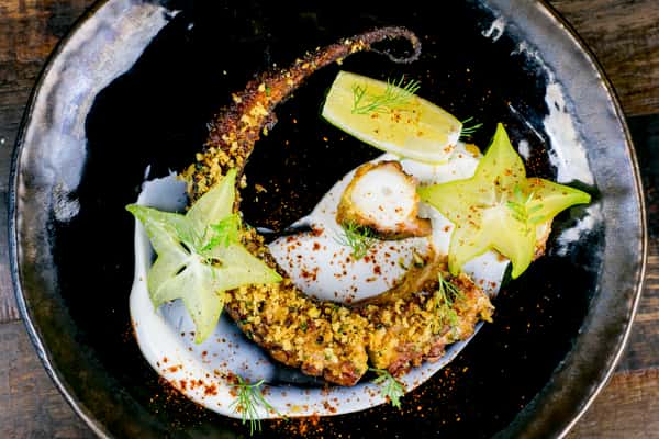 Grilled octopus plated with creamy sauce, starfruit, and fresh herbs in a fine dining seafood presentation