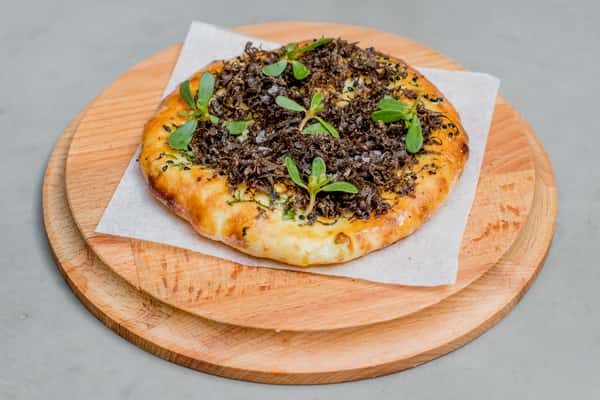 Wood-fired flatbread topped with shaved black truffles, fresh microgreens, and sea salt on a wooden serving board