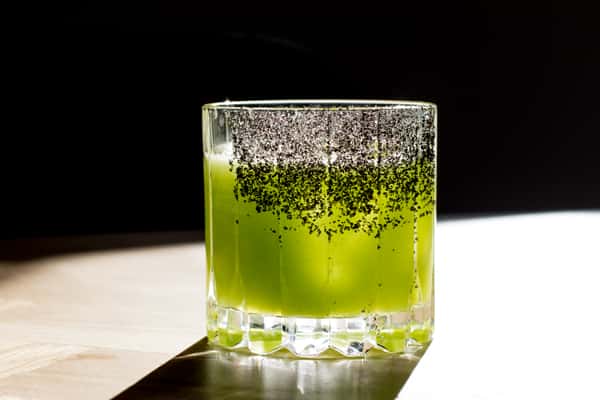 Bright green handcrafted cocktail with a dark sugar rim served in a crystal rocks glass