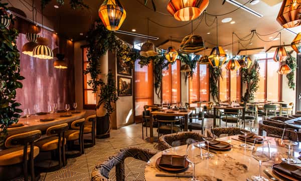 Elegant restaurant dining room with warm pendant lighting, marble tables, and lush greenery accents