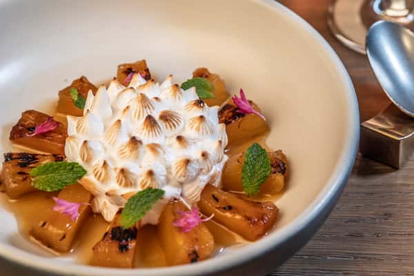 Caramelized pineapple dessert topped with toasted meringue, fresh mint, and edible flowers in an elegant fine dining presentation