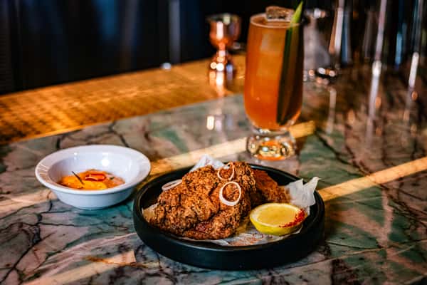 Crispy fried chicken served with creamy dipping sauce and a handcrafted cocktail on a marble bar top in an upscale restaurant lounge