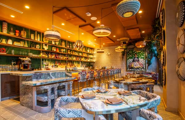 Stylish restaurant bar and dining room with marble tables, patterned seating, and warm designer lighting