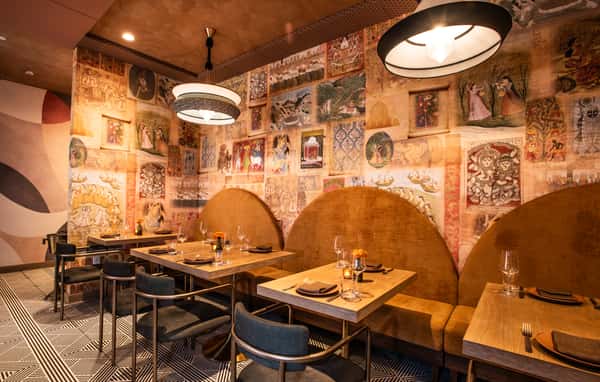 Intimate restaurant booth seating with artistic mural walls, modern pendant lighting, and contemporary table settings