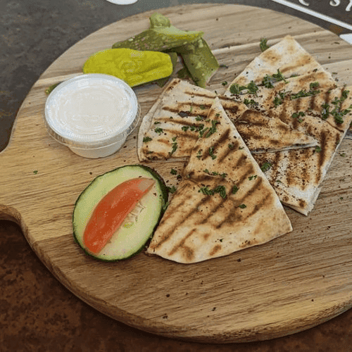 Grilled chicken shawarma wrap served with garlic sauce, pickles, tomato slices, and lemon wedges on a wooden board.