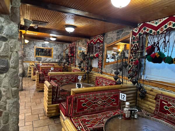 Cozy Mediterranean restaurant interior with wooden log seating, vibrant red patterned cushions, and colorful hanging mosaic lamps.
