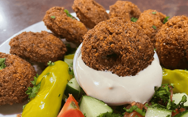Crispy falafel served with creamy tahini sauce, fresh cucumber, tomatoes, parsley, and pickled peppers for a Mediterranean flavor.