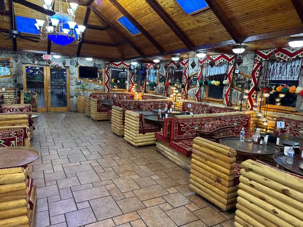 Cozy Mediterranean restaurant interior with wooden log seating, vibrant red patterned cushions, and colorful hanging mosaic lamps.