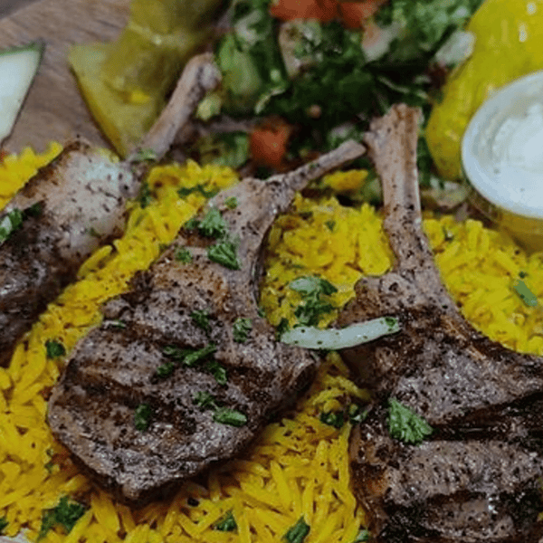 Grilled lamb chops served on fragrant yellow rice, garnished with fresh parsley and accompanied by a side salad and pickled vegetables.