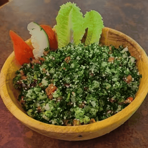 Fresh tabbouleh salad with finely chopped parsley, tomatoes, bulgur, and onions, garnished with lettuce, cucumber, and tomato wedges.