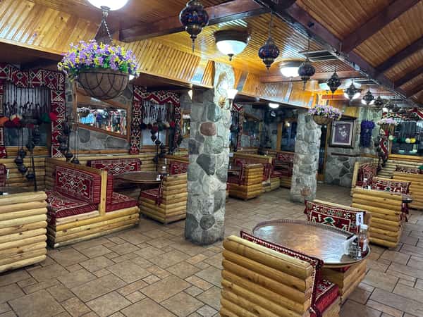 Cozy Mediterranean restaurant interior with wooden log seating, vibrant red patterned cushions, and colorful hanging mosaic lamps.