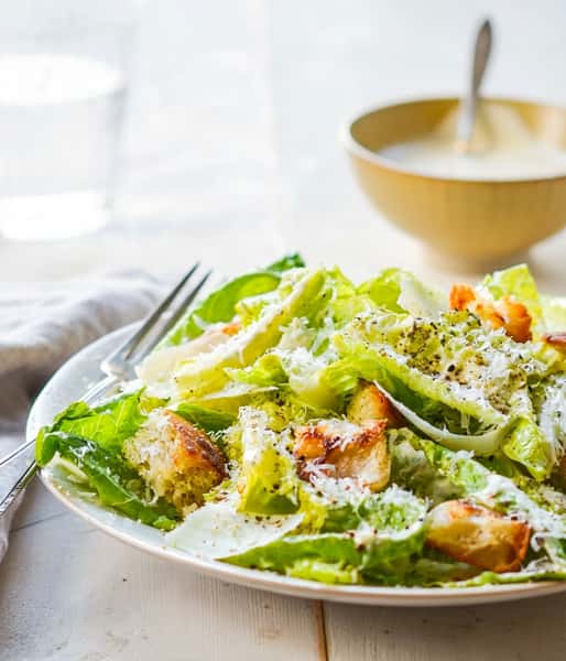 Fresh romaine lettuce with croutons, grated parmesan, and creamy Caesar dressing on a white plate.
