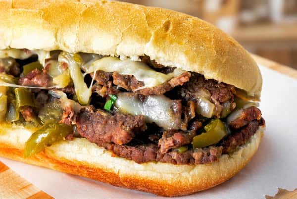Philly cheesesteak sandwich with sliced beef, melted cheese, and peppers on a hoagie roll.