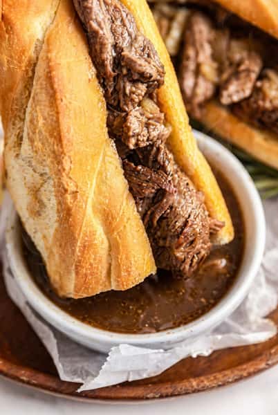 Sliced roast beef sandwich on a toasted roll served with a cup of au jus for dipping.