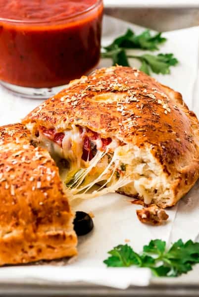 Golden-brown baked calzone filled with melted cheese and vegetables, served with a side of marinara sauce.