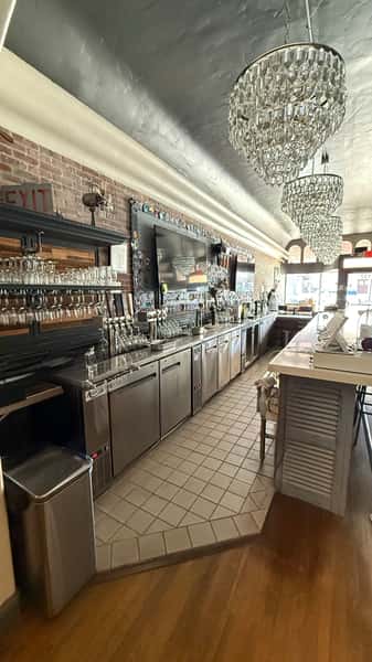 Elegant bar interior with crystal chandeliers, stainless steel counters, rows of taps, and neatly arranged glassware along the wall.