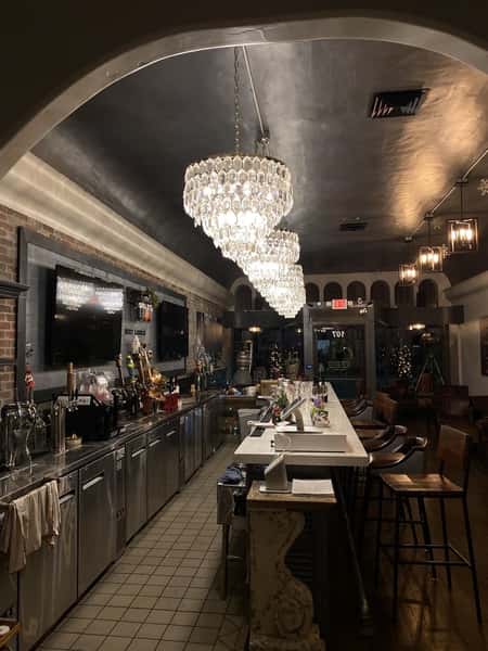 Elegant bar interior with crystal chandeliers, high stools, and stainless steel counters creating a warm evening ambiance.