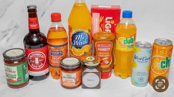 A collection of assorted Irish food and drink products arranged on a table, including sauces, relishes, curry sauce, crackers, soft drinks, wine cooler, and a bottle of Smithwick's Irish Red Ale.