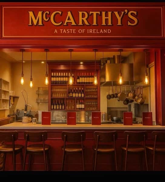 Bright red McCarthy's – A Taste of Ireland restaurant bar with warm pendant lighting, bar stools along the counter, and an open kitchen with copper pots and shelves of wine bottles