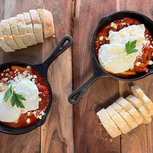 Cast iron skillet of Two Poached Eggs over a Tomato Sauce of Spanish Paprika & Cumin, Cayenne, Red Bell Pepper, Garlic, Onion + Warm Baguette