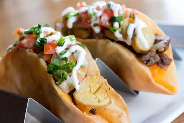 two tacos with scallions, a white sauce, and tomatoes on top