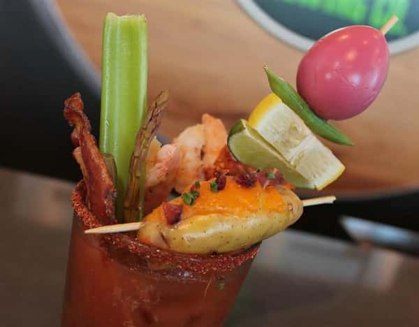 a bloody mary with bacon, celery, lemon, lime, and a tomato on top
