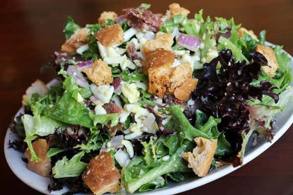 a salad with onions, crutons, cheese on top